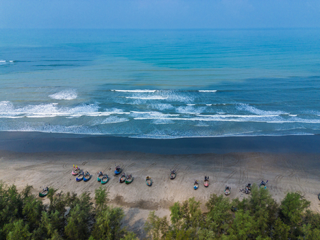 Aerial view of traditional fishing boats parked on the sandy shore with waves crashing on the beach and lush green trees Cox s Bazar Chittagong Division Bangladesh. Aerial view of traditional fishing boats parked on the sandy shore with waves crashing on the beach and lush green trees Cox s Bazar Chittagong Division Bangladesh.