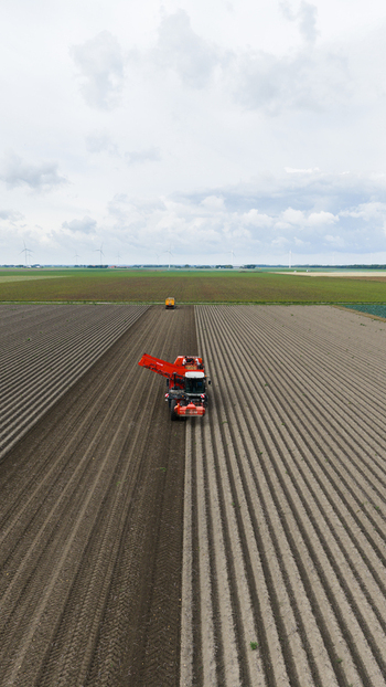 Aerial view of a red potato harvester working in a large plowed field with wind turbines in the distance in Zeewolde Flevoland Netherlands. Aerial view of a red potato harvester working in a large plowed field with wind turbines in the distance in Zeewolde Flevoland Netherlands.