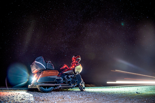 View of a motorcycle parked on a gravel road under a starry night sky with light trails in Algeria.
