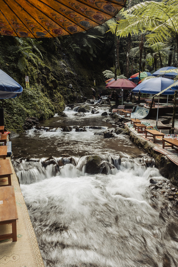View of Grojogan Sewu Loket 2 featuring a cascading river surrounded by lush tropical ferns and colorful umbrellas over seating areas in Kecamatan Tawangmangu Jawa Tengah Indonesia.