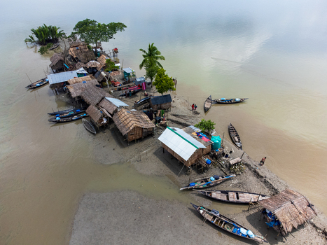 Aerial view of Kalabagi village with thatched roof huts on a narrow strip of land and wooden boats moored on the muddy banks in Khulna District Khulna Division Bangladesh.