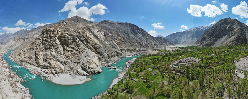 Aerial view of the Gol Valley with the turquoise Indus River flowing through lush green fields and rocky mountains in Skardu Gilgit Baltistan Pakistan.