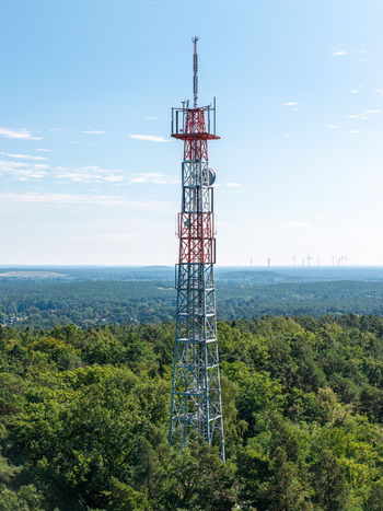 Aerial view of Muggelberge Antenne radio antenna rising above the dense green forest canopy under a clear blue sky Berlin Berlin Germany. Aerial view of Muggelberge Antenne radio antenna rising above the dense green forest canopy under a clear blue sky Berlin Berlin Germany.