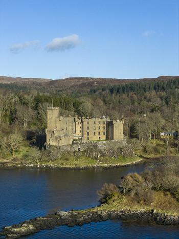Aerial view of Dunvegan Castle on a rocky cliff overlooking the sea loch surrounded by dense woodland and rolling hills in Isle of Skye Scotland United Kingdom. Aerial view of Dunvegan Castle on a rocky cliff overlooking the sea loch surrounded by dense woodland and rolling hills in Isle of Skye Scotland United Kingdom.
