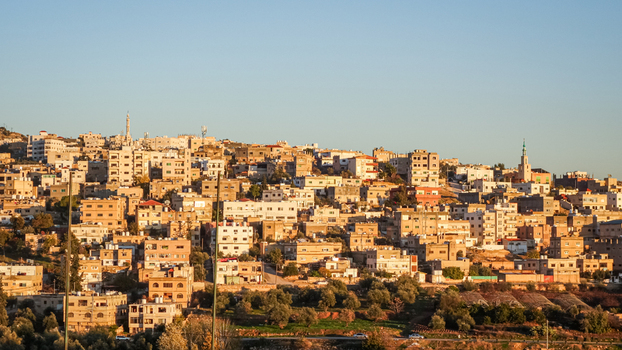 View of the historic city of Jerash with its dense stone architecture minarets and surrounding olive groves under a clear sky in Jerash Jerash Governorate Jordan. View of the historic city of Jerash with its dense stone architecture minarets and surrounding olive groves under a clear sky in Jerash Jerash Governorate Jordan.