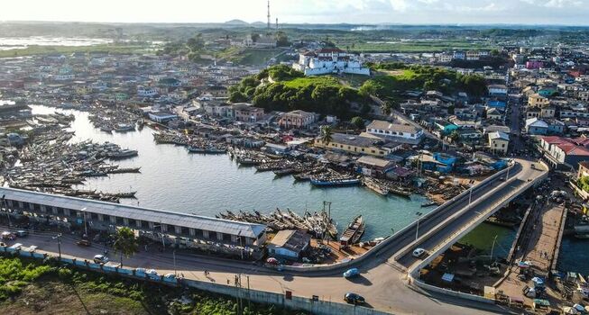 Aerial view of Cape Coast Castle overlooking the fishing harbour with numerous wooden boats docked along the shore and a bridge spanning the water in Ghana. Aerial view of Cape Coast Castle overlooking the fishing harbour with numerous wooden boats docked along the shore and a bridge spanning the water in Ghana.