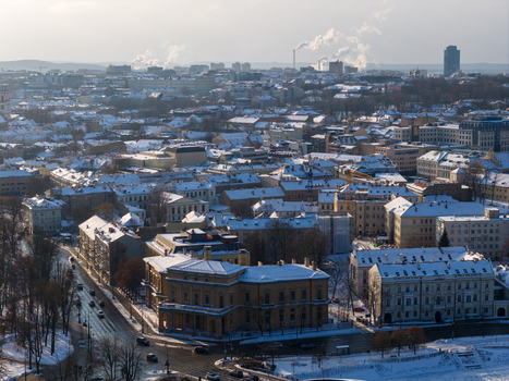 Aerial view of snow covered rooftops and historic buildings under a soft winter light with smoke rising from distant chimneys Vilnius County Lithuania.