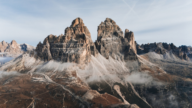 Aerial view of Tre Cime di Lavaredo with its iconic jagged limestone peaks rising above low clouds and winding mountain paths Auronzo di Cadore Veneto Italy. Aerial view of Tre Cime di Lavaredo with its iconic jagged limestone peaks rising above low clouds and winding mountain paths Auronzo di Cadore Veneto Italy.