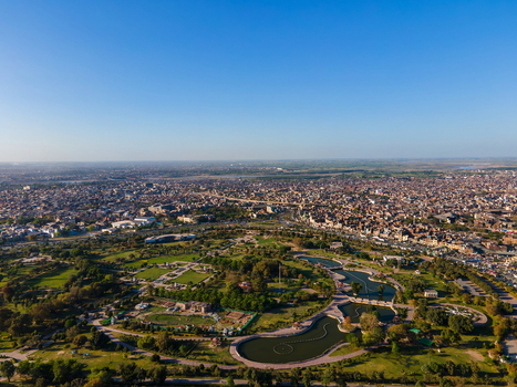 Aerial view of Minar e Pakistan and Greater Iqbal Park with green lawns winding pathways and water features set against the dense urban skyline of Lahore Punjab Pakistan.