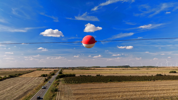 Aerial view of a red and white aerial marker ball on a power line overlooking a rural landscape with a road cars and wind turbines in the distance in Bavaniste Vojvodina Serbia. Aerial view of a red and white aerial marker ball on a power line overlooking a rural landscape with a road cars and wind turbines in the distance in Bavaniste Vojvodina Serbia.