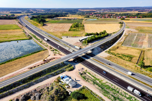 Aerial view of a highway overpass with trucks and cars driving through rural fields and a small pond in Hochstadt Bavaria Germany. Aerial view of a highway overpass with trucks and cars driving through rural fields and a small pond in Hochstadt Bavaria Germany.