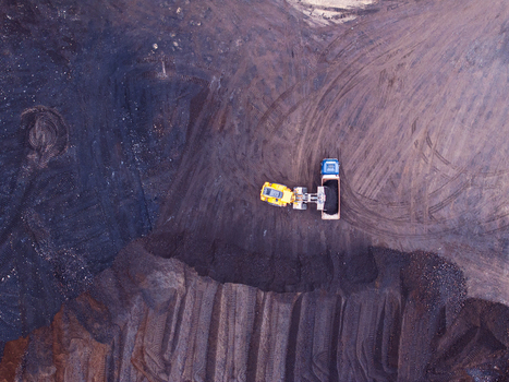 Aerial view of a yellow front end loader and a blue dump truck working in a dark mining site with tire tracks on the ground in Iceland. Aerial view of a yellow front end loader and a blue dump truck working in a dark mining site with tire tracks on the ground in Iceland.
