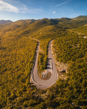 Aerial view of a winding mountain road with a sharp hairpin turn surrounded by lush green hills and rocky peaks under a clear blue sky Rijeka Primorje Gorski Kotar Croatia. Aerial view of a winding mountain road with a sharp hairpin turn surrounded by lush green hills and rocky peaks under a clear blue sky Rijeka Primorje Gorski Kotar Croatia.