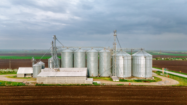 Aerial view of a cluster of silver silos gleaming against the brown earth and green fields under a vast cloudy sky Sremska Mitrovica Vojvodina Serbia. Aerial view of a cluster of silver silos gleaming against the brown earth and green fields under a vast cloudy sky Sremska Mitrovica Vojvodina Serbia.