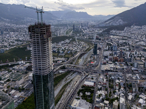 Aerial view of the Rise Tower skyscraper under construction with a crane on top surrounded by the urban landscape highways and mountains in Monterrey Nuevo Leon Mexico. Aerial view of the Rise Tower skyscraper under construction with a crane on top surrounded by the urban landscape highways and mountains in Monterrey Nuevo Leon Mexico.