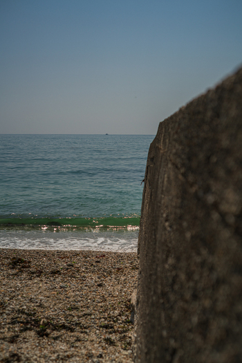 View of a concrete wall bordering a pebble beach with calm sea waves under a clear blue sky in Charlestown Cornwall United Kingdom. View of a concrete wall bordering a pebble beach with calm sea waves under a clear blue sky in Charlestown Cornwall United Kingdom.