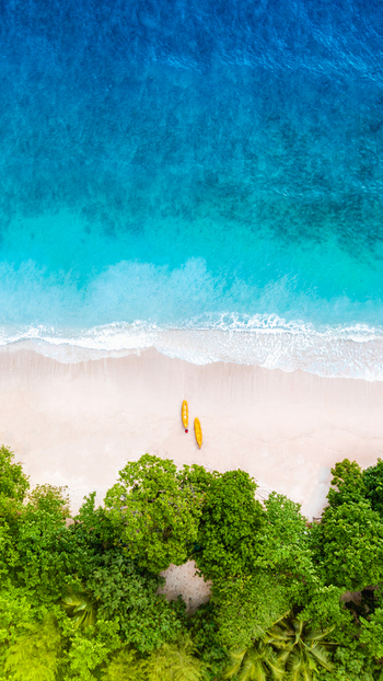Aerial view of Pantai Gatra with two yellow kayaks resting on the white sand beach bordered by lush green tropical trees and turquoise ocean water in Malang Regency East Java Indonesia. Aerial view of Pantai Gatra with two yellow kayaks resting on the white sand beach bordered by lush green tropical trees and turquoise ocean water in Malang Regency East Java Indonesia.