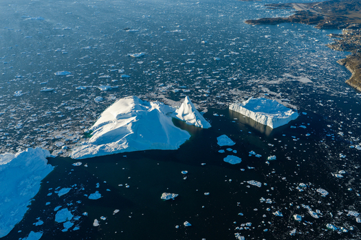 Aerial view of Ilulissat glacier with massive icebergs floating in dark blue arctic waters near the rugged coastline of Greenland. Aerial view of Ilulissat glacier with massive icebergs floating in dark blue arctic waters near the rugged coastline of Greenland.