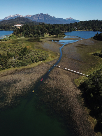 Aerial view of kayakers paddling through a narrow channel in Nahuel Huapi Lake surrounded by lush forests and mountains in San Carlos de Bariloche Rio Negro Argentina. Aerial view of kayakers paddling through a narrow channel in Nahuel Huapi Lake surrounded by lush forests and mountains in San Carlos de Bariloche Rio Negro Argentina.