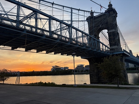 View of the John A. Roebling Suspension Bridge spanning the Ohio River at sunset with a stadium in the background Covington Kentucky United States.
