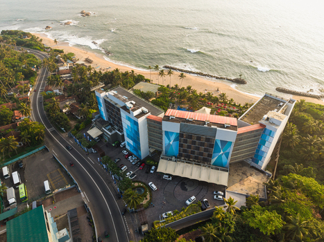 Aerial view of a modern beachfront hotel complex situated along a winding coastal road with sandy shores and ocean waves in Galle Southern Province Sri Lanka.
