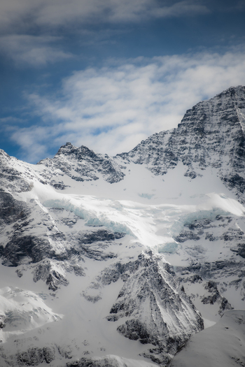 View of snow capped mountains reaching into the sky contrasting with the deep blue sky and light clouds creating a sense of altitude Murren Switzerland. View of snow capped mountains reaching into the sky contrasting with the deep blue sky and light clouds creating a sense of altitude Murren Switzerland.