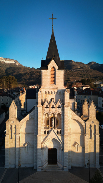 Aerial view of the Eglise Saint Pierre with its stone facade and tall spire against a backdrop of mountains in Gex Auvergne Rhone Alpes France. Aerial view of the Eglise Saint Pierre with its stone facade and tall spire against a backdrop of mountains in Gex Auvergne Rhone Alpes France.
