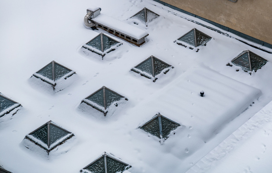 View of a snow covered roof featuring multiple pyramid shaped glass skylights and light footprints in the fresh winter snow in Vilnius Vilnius County Lithuania. View of a snow covered roof featuring multiple pyramid shaped glass skylights and light footprints in the fresh winter snow in Vilnius Vilnius County Lithuania.