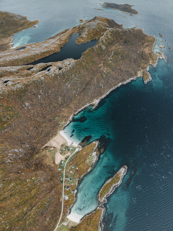 Aerial view of the rugged coastline and turquoise waters of Senja island featuring rocky terrain small coastal houses and a winding road in Senja Troms Norway.