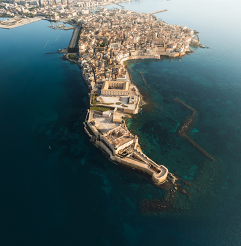 Aerial view of the Island of Ortigia and Maniace Castle surrounded by the turquoise Mediterranean Sea and historic stone architecture in Syracuse Sicily Italy.