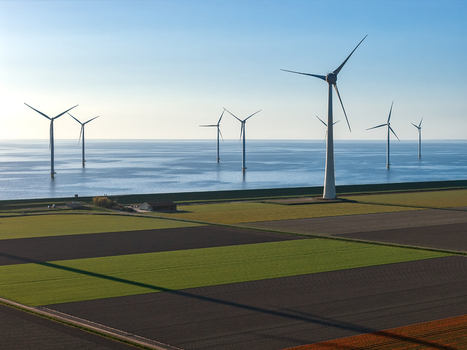Aerial view of wind turbines standing in the sea and along agricultural fields under a clear blue sky Netherlands.