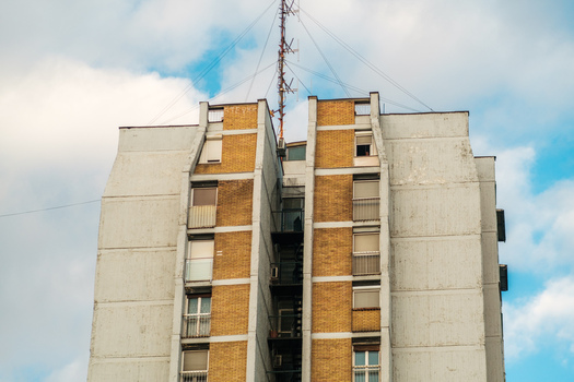 View of a tall residential apartment building with yellow brick facade concrete balconies and a radio antenna on the roof in Novi Sad Vojvodina Serbia. View of a tall residential apartment building with yellow brick facade concrete balconies and a radio antenna on the roof in Novi Sad Vojvodina Serbia.