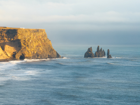 Aerial view of the dramatic Dyrholaey cliffs and basalt sea stacks rising from the Atlantic Ocean under soft golden light in Myrdalshreppur Iceland. Aerial view of the dramatic Dyrholaey cliffs and basalt sea stacks rising from the Atlantic Ocean under soft golden light in Myrdalshreppur Iceland.