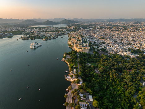 Aerial view of the historic City Palace complex situated on the banks of Lake Pichola surrounded by lush gardens and the urban landscape of Udaipur Rajasthan India.