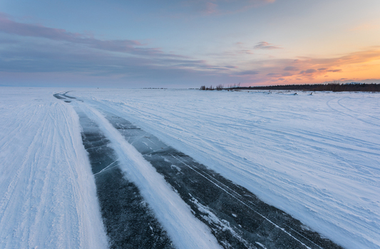 View of Lake Baikal covered in thick ice with tire tracks leading into the distance under a soft sunset sky in Severobaykalsk Buryatia Russia. View of Lake Baikal covered in thick ice with tire tracks leading into the distance under a soft sunset sky in Severobaykalsk Buryatia Russia.