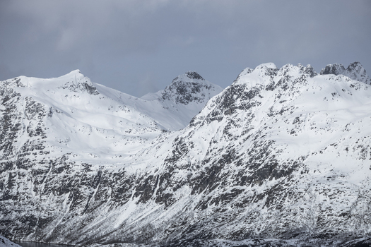 View of snow covered mountain peaks and rugged ridges under a cloudy winter sky in Ersfjord Troms Norway. View of snow covered mountain peaks and rugged ridges under a cloudy winter sky in Ersfjord Troms Norway.