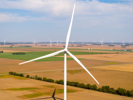 Aerial view of a large wind turbine in a vast agricultural field with rows of turbines stretching into the horizon under a clear sky in Wolcott Indiana United States.