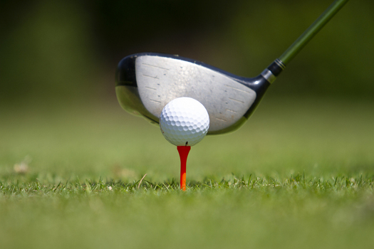View of a white golf ball resting on a red tee with a driver club positioned for a swing on a lush green course in Tiwi Wilaya ya Kwale Kenya. View of a white golf ball resting on a red tee with a driver club positioned for a swing on a lush green course in Tiwi Wilaya ya Kwale Kenya.