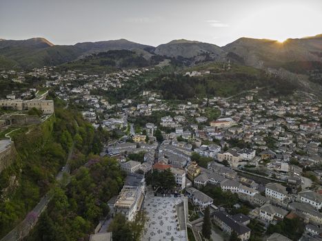 Aerial view of Gjirokaster Fortress overlooking the historic stone city with traditional slate roofed houses and surrounding mountains at sunset in Gjirokaster Gjirokaster County Albania. Aerial view of Gjirokaster Fortress overlooking the historic stone city with traditional slate roofed houses and surrounding mountains at sunset in Gjirokaster Gjirokaster County Albania.