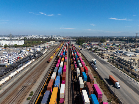 Aerial view of a busy railyard filled with colorful shipping containers on freight trains adjacent to industrial roads and warehouses in Carson California United States.