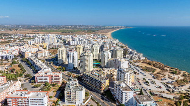 Aerial view of the coastal town of Armacao de Pera with its high rise apartment buildings sandy beach and the Atlantic Ocean under a clear blue sky in Armacao de Pera Faro District Portugal. Aerial view of the coastal town of Armacao de Pera with its high rise apartment buildings sandy beach and the Atlantic Ocean under a clear blue sky in Armacao de Pera Faro District Portugal.