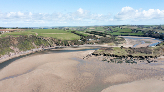 Aerial view of Bantham Beach featuring the sandy estuary rugged cliffs and rolling green hills under a blue sky with scattered clouds in Kingsbridge Devon United Kingdom. Aerial view of Bantham Beach featuring the sandy estuary rugged cliffs and rolling green hills under a blue sky with scattered clouds in Kingsbridge Devon United Kingdom.