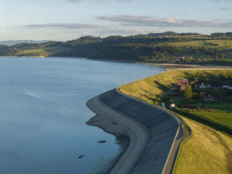 Aerial view of Lake Czorsztynskie with its concrete dam embankment calm blue water and surrounding green hills under soft golden hour light in Nowy Targ Lesser Poland Voivode Poland.