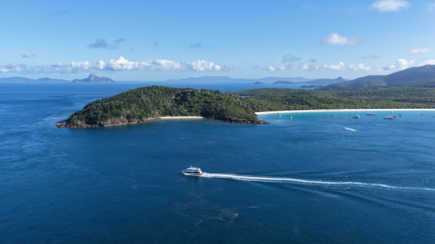 Aerial view of Haslewood Island featuring a boat cruising through turquoise waters white sandy beaches and lush tropical vegetation in Whitsundays Queensland Australia. Aerial view of Haslewood Island featuring a boat cruising through turquoise waters white sandy beaches and lush tropical vegetation in Whitsundays Queensland Australia.