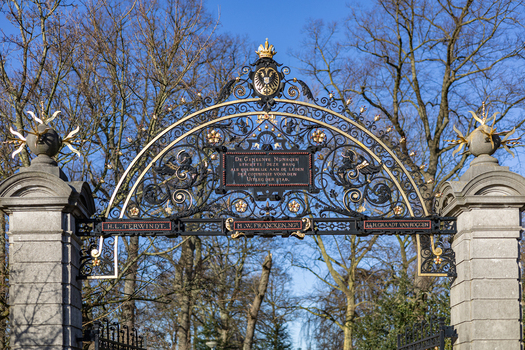 View of the ornate wrought iron gate of the Voetgangersbrug Kelfkensbosch with gold accents and stone pillars under a clear blue sky Nijmegen Gelderland Netherlands. View of the ornate wrought iron gate of the Voetgangersbrug Kelfkensbosch with gold accents and stone pillars under a clear blue sky Nijmegen Gelderland Netherlands.