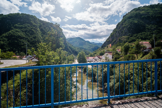View of the town of Savnik nestled in a lush green valley between mountains in Montenegro seen from a bridge with a blue railing. Savnik Savnik Municipality Montenegro.