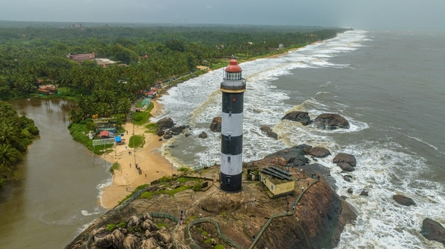 Aerial view of Kapu Light House standing on a rocky promontory surrounded by crashing waves sandy beaches and lush palm trees along the coastline in Udupi Karnataka India.