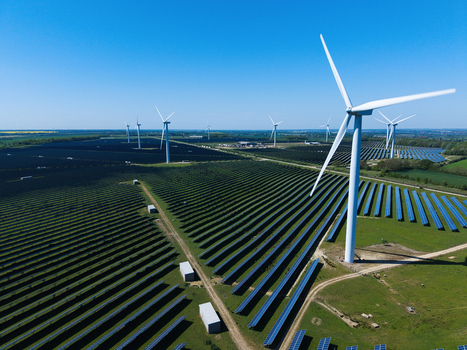 Aerial view of Chelveston Wind Farm featuring rows of solar panels and tall wind turbines under a clear blue sky in Wellingborough England United Kingdom. Aerial view of Chelveston Wind Farm featuring rows of solar panels and tall wind turbines under a clear blue sky in Wellingborough England United Kingdom.