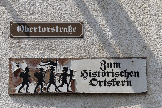 View of street signs on a textured wall including a sign for Obertorstrasse and a directional sign with medieval soldier illustrations Monreal Rhineland Palatinate Germany. View of street signs on a textured wall including a sign for Obertorstrasse and a directional sign with medieval soldier illustrations Monreal Rhineland Palatinate Germany.