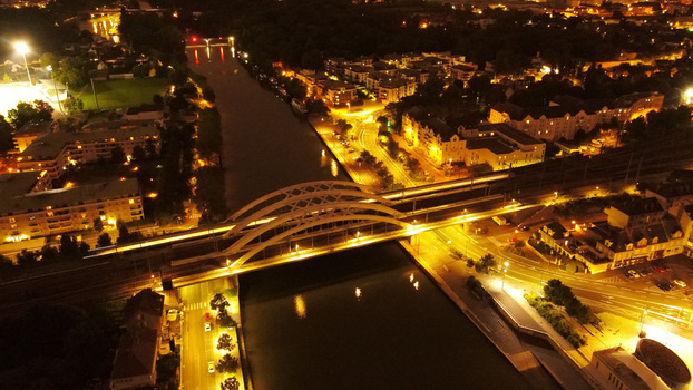 Aerial view of the illuminated bridge over the Oise River at night with street lights reflecting on the water and surrounding urban buildings in Pontoise Ile de France France. Aerial view of the illuminated bridge over the Oise River at night with street lights reflecting on the water and surrounding urban buildings in Pontoise Ile de France France.